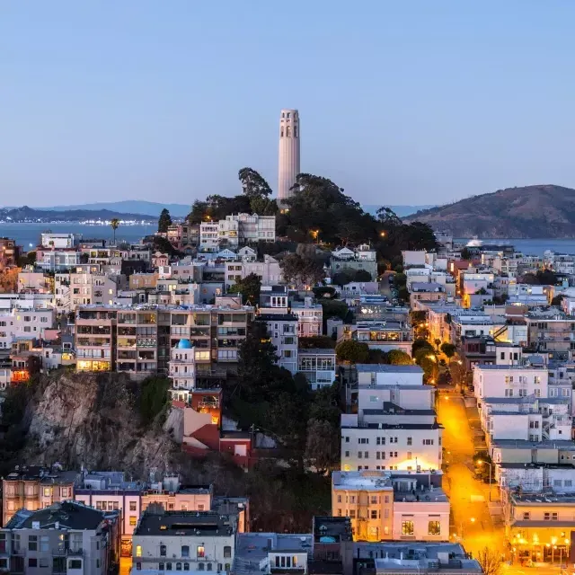 贝博体彩app科伊特塔日落时分, con le strade illuminate davanti e la baia di San Francisco alle spalle.